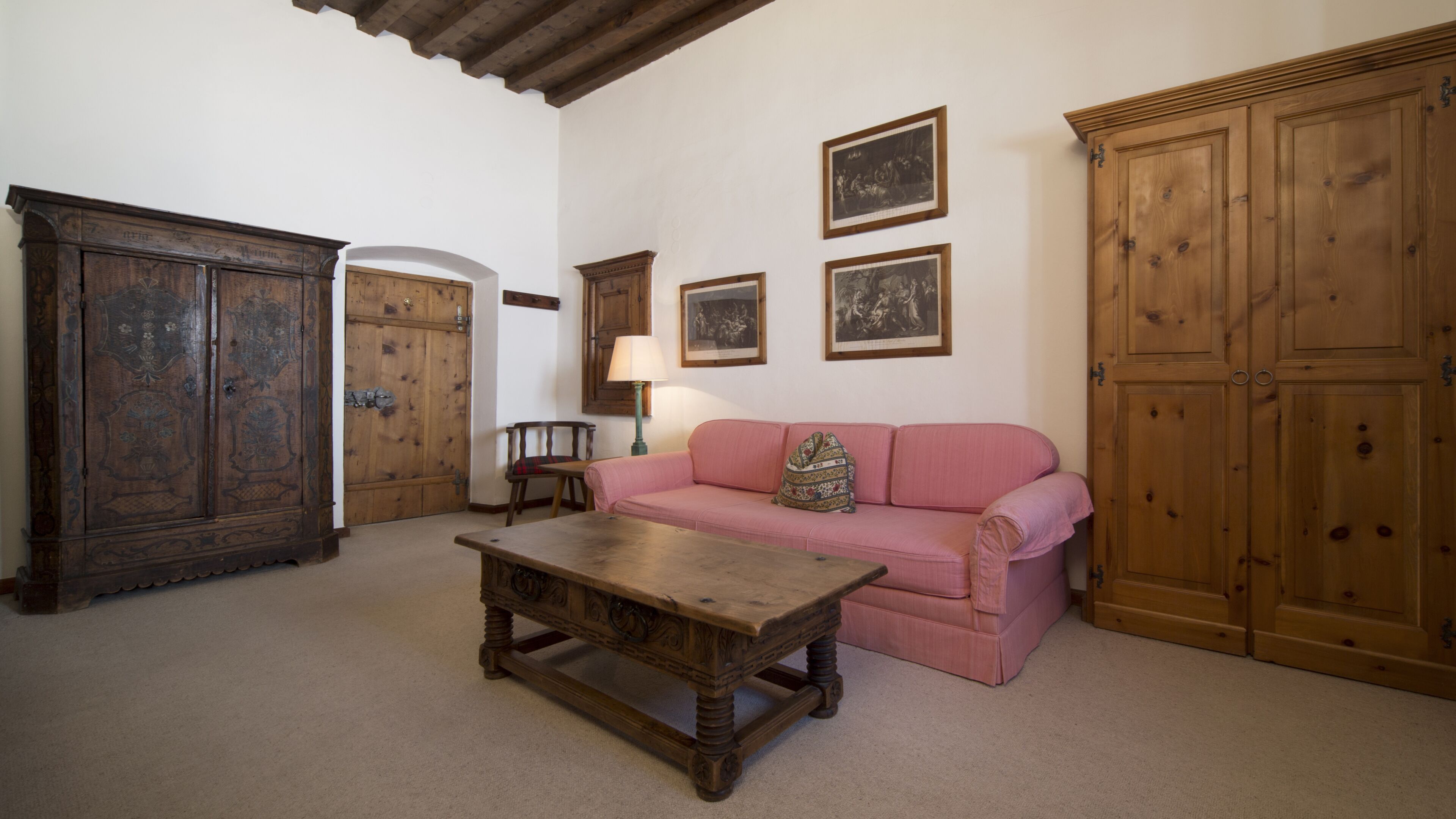 A room with a wooden table, a pink sofa, and two wooden cabinets.