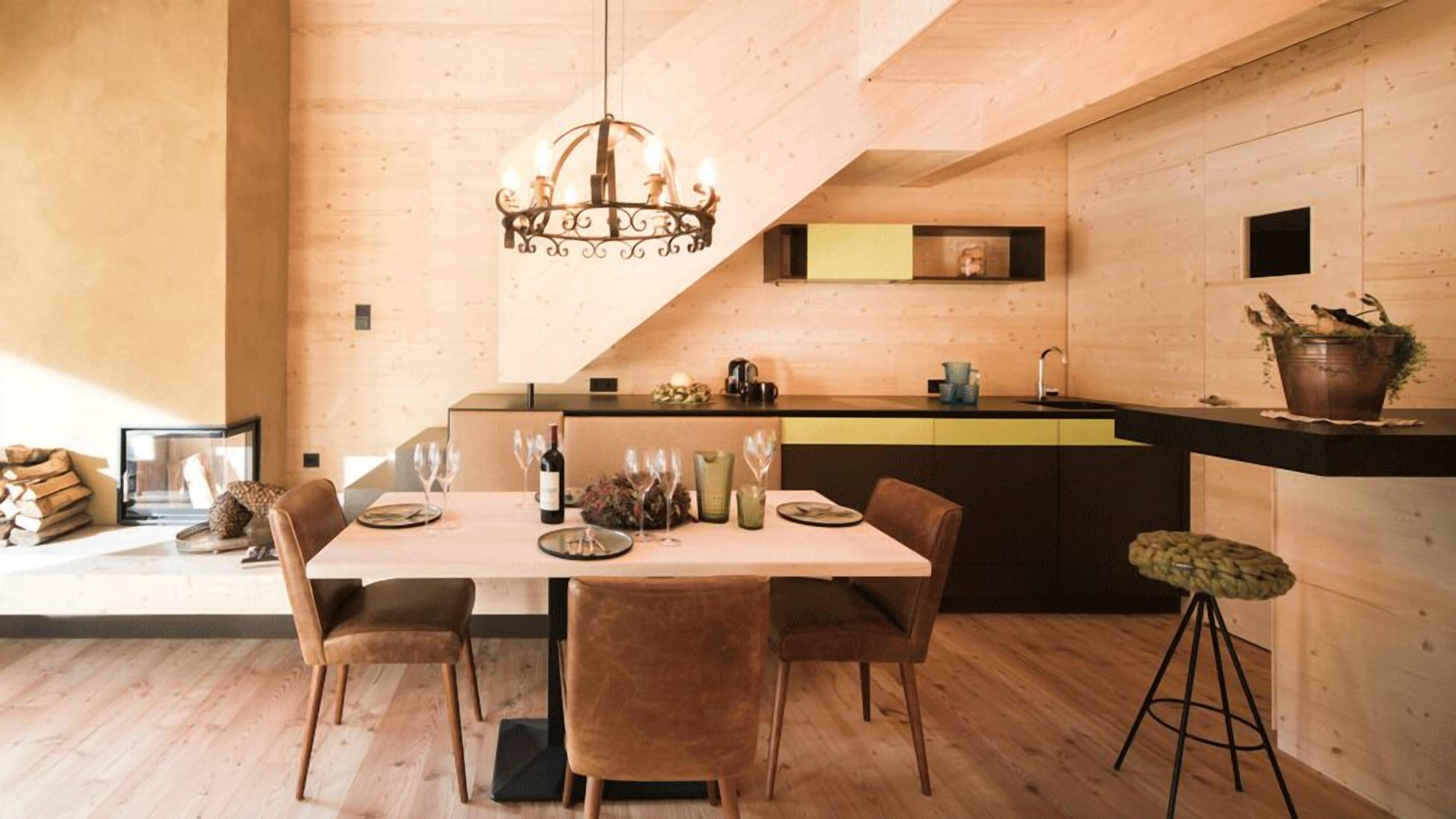 A modern kitchen with a wooden interior, a dining table set with glasses and plates, and a hanging light fixture.