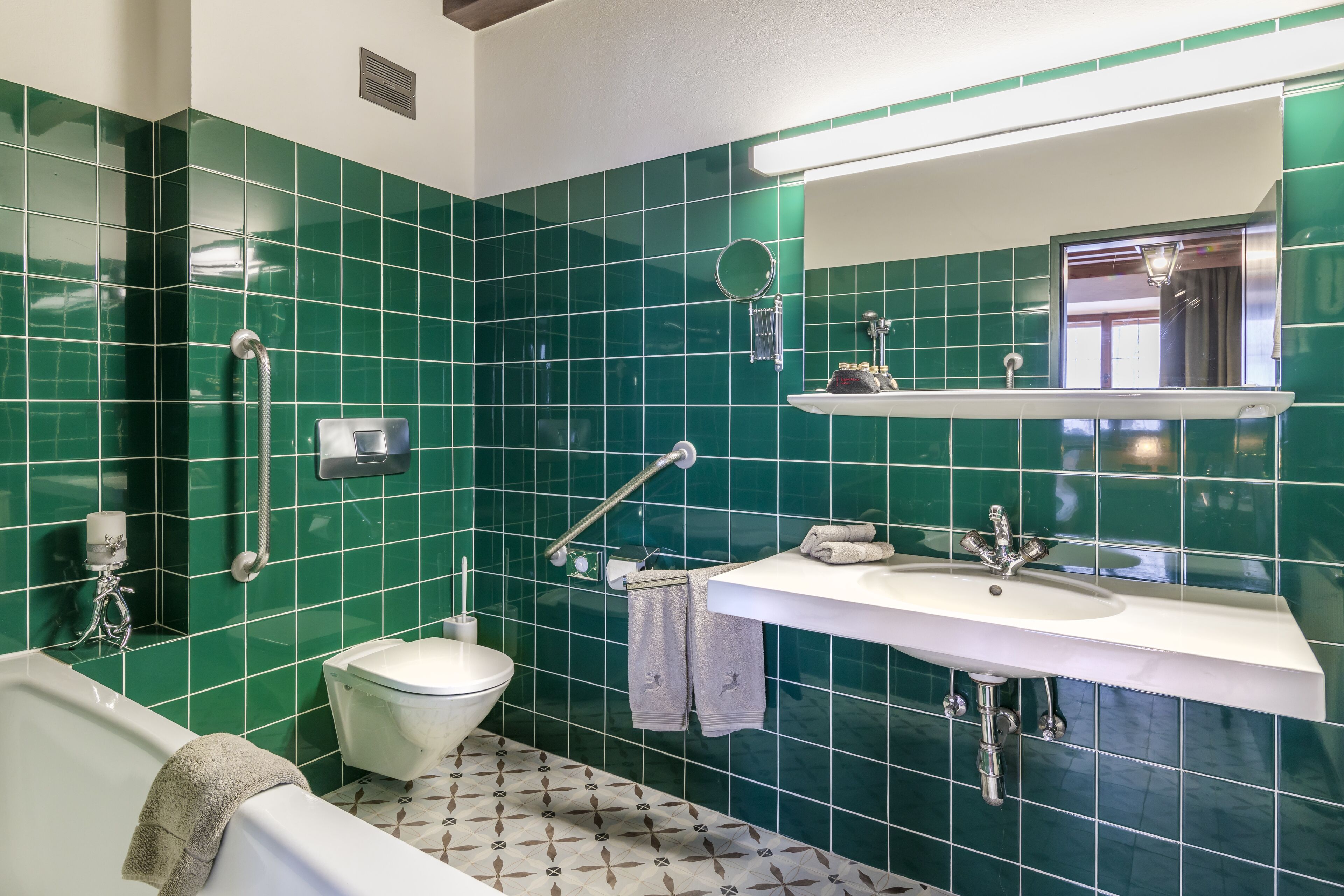 A bathroom with green tiles, a white sink, a toilet, a bathtub, and a mirror.