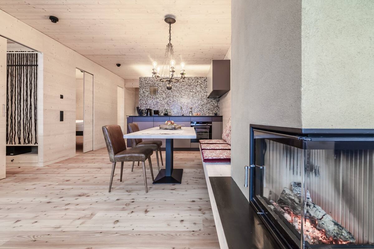 A modern kitchen with a brick backsplash, a dining area with a table and chairs, and a fireplace with burning logs.