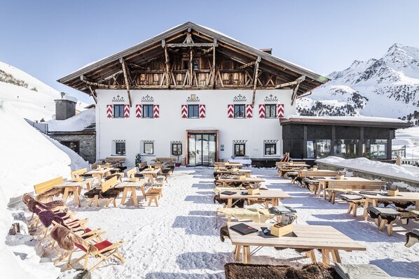 A building with a wooden facade and a snow-covered outdoor seating area with wooden tables and benches. - Hotel Jagdschloss Resort (Silz)