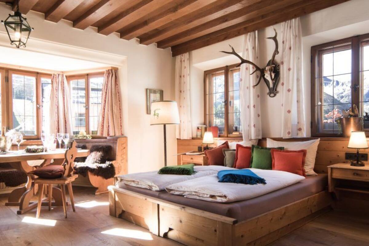 A cozy room with a wooden bed, a desk with a chair, and large windows with curtains.