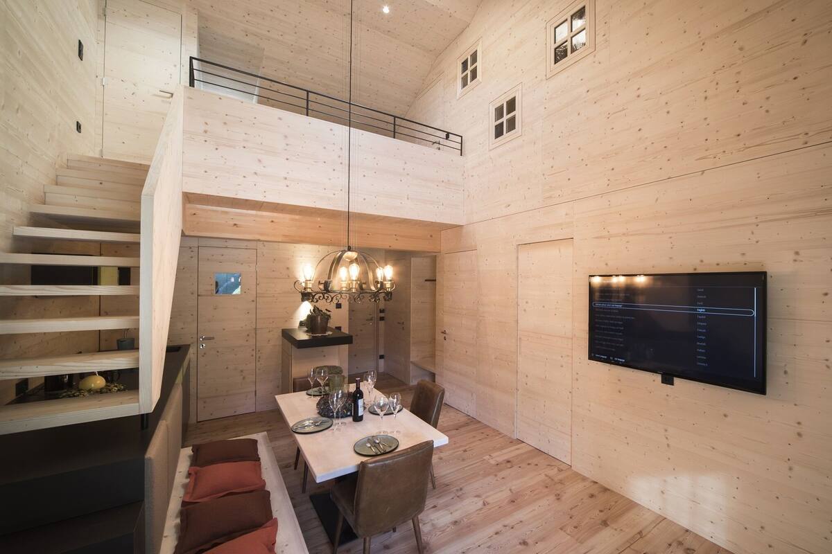 A wooden interior with a dining area, a staircase, and a mounted television.