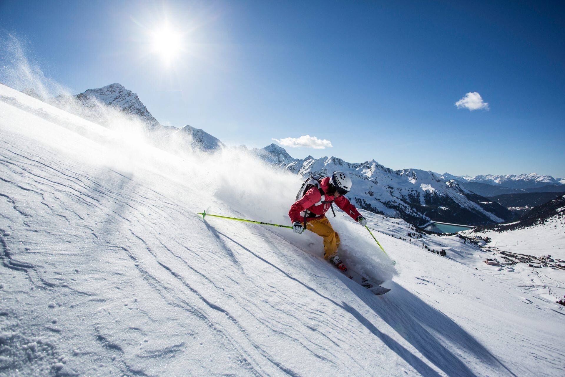 Een skiër op een besneeuwde helling, met daarin de achtergrond van een berglandschap en een heldere lucht.