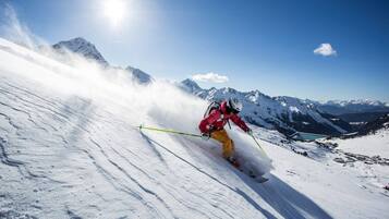 Een skiër op een besneeuwde helling, met daarin de achtergrond van een berglandschap en een heldere lucht.