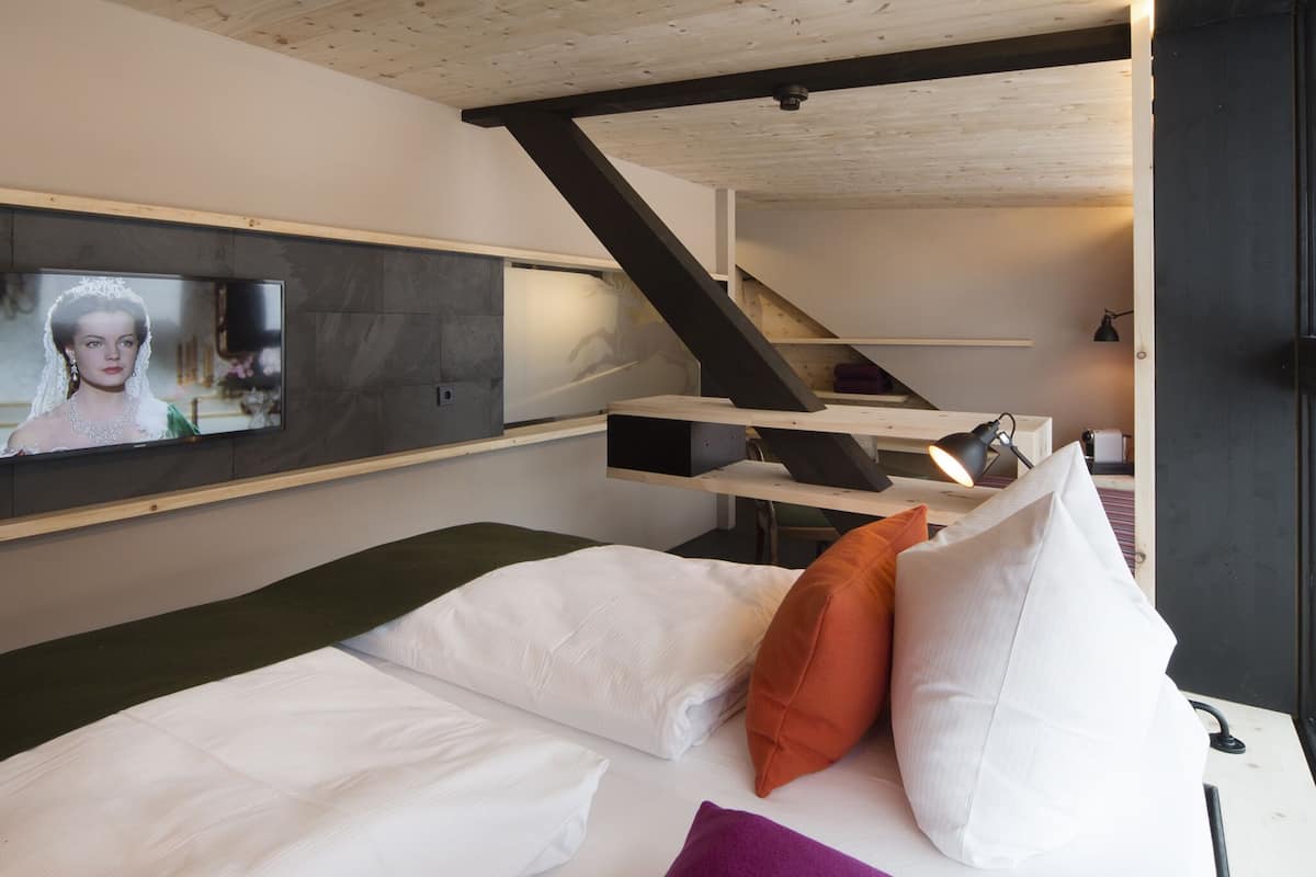 A modern room with a bed, a TV mounted on the wall, and a staircase leading to an upper level.