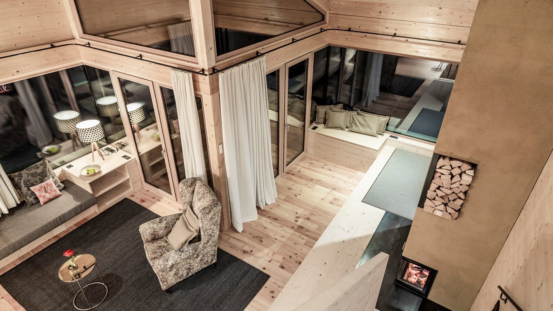 A modern log cabin interior with a cozy seating area, a fireplace, and large windows.