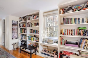 A room with multiple bookshelves filled with books, a framed picture on the wall, and a small table with a chair.