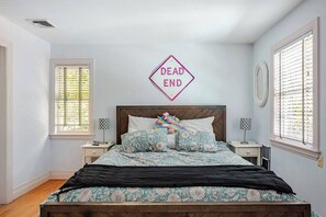 A bedroom with a bed, two bedside tables, a window with blinds, and a wall-mounted sign. - 5 bedroom Private Family Get Away w/ Heated Pool (Westhampton Beach)