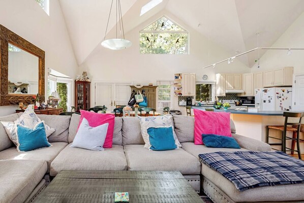 A spacious living room with a large sofa, a coffee table, and a view of the kitchen and dining area.