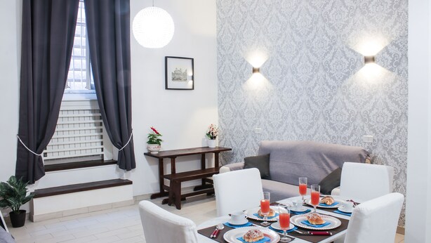 A dining area with a table set for breakfast, a sofa, a staircase, and a patterned wall. - Chroma Apt Farinone 28 (Rome)