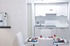 A modern kitchen with white cabinets, a sink, and a dining area with two white chairs and a table set for breakfast.