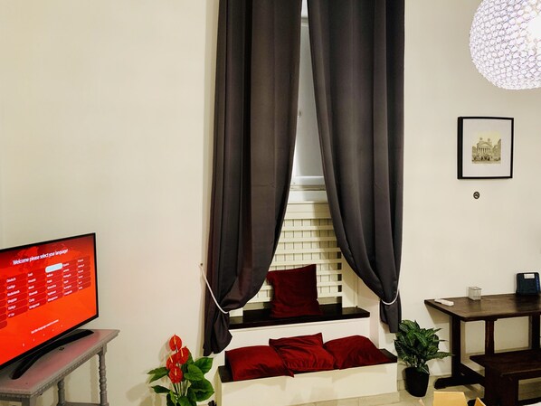 A modern living room with a television displaying a language selection screen, a staircase with red cushions, a potted plant, and a framed picture on the wall.