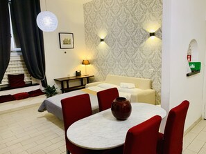 A hotel room with a bed, a desk, a lamp, a vase, and a dining table with chairs.
