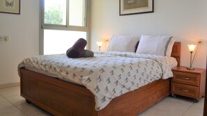 A bedroom with a wooden bed, a window, a nightstand with a lamp, and framed artwork on the walls. - 2BDR Amazing Location with Parking (Tel Aviv)