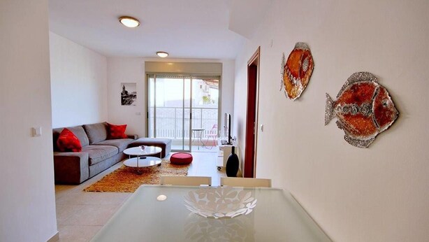A modern living room with a sofa, coffee table, and decorative fish wall art. - 2BDR Amazing Location with Parking (Tel Aviv)