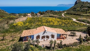Una villa blanca con techo de tejas, rodeada de un jardín y vistas al mar.