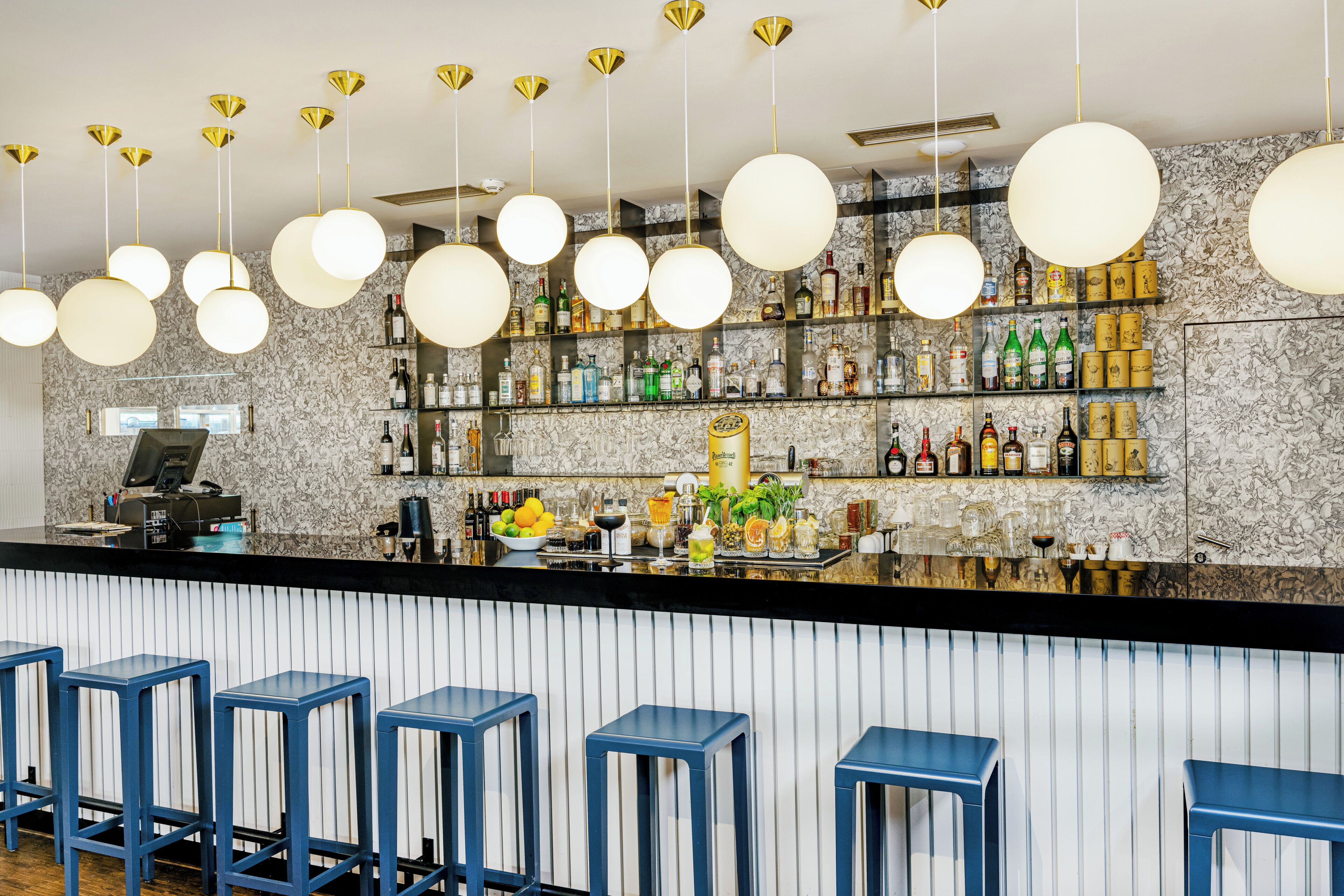 A bar area with multiple stools, hanging spherical light fixtures, and shelves stocked with bottles.