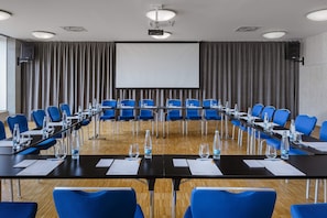 A conference room with a long table, blue chairs, water bottles, and a projector screen.