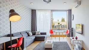 Una sala moderna con un sofá seccional, una mesa de comedor con sillas, una lámpara de pie y un ventanal con cortinas.
