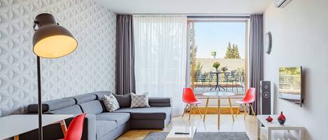 A modern living room with a sectional sofa, a dining table with chairs, a floor lamp, and a large window with curtains.