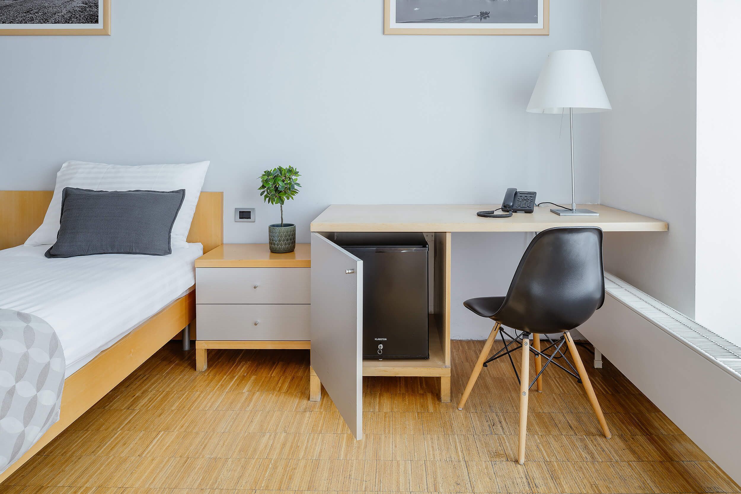 Un dormitorio con cama, escritorio, silla, planta pequeña y radiador.
