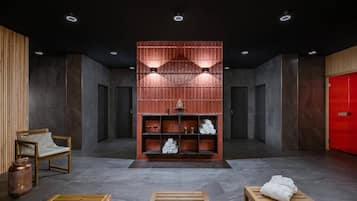 A modern lobby with a central wooden bench, a seating area with a chair, a red wall with shelves, and a red door.