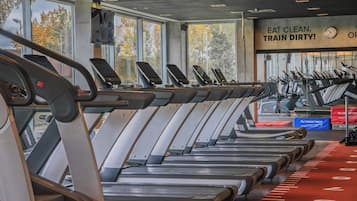 Un gimnasio con cintas de correr alineadas, una pista de atletismo roja y un cartel motivacional en la pared.