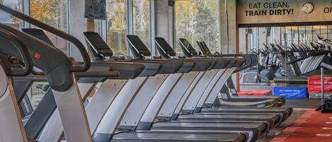 A gym with treadmills aligned in rows, a red running track, and a motivational poster on the wall.