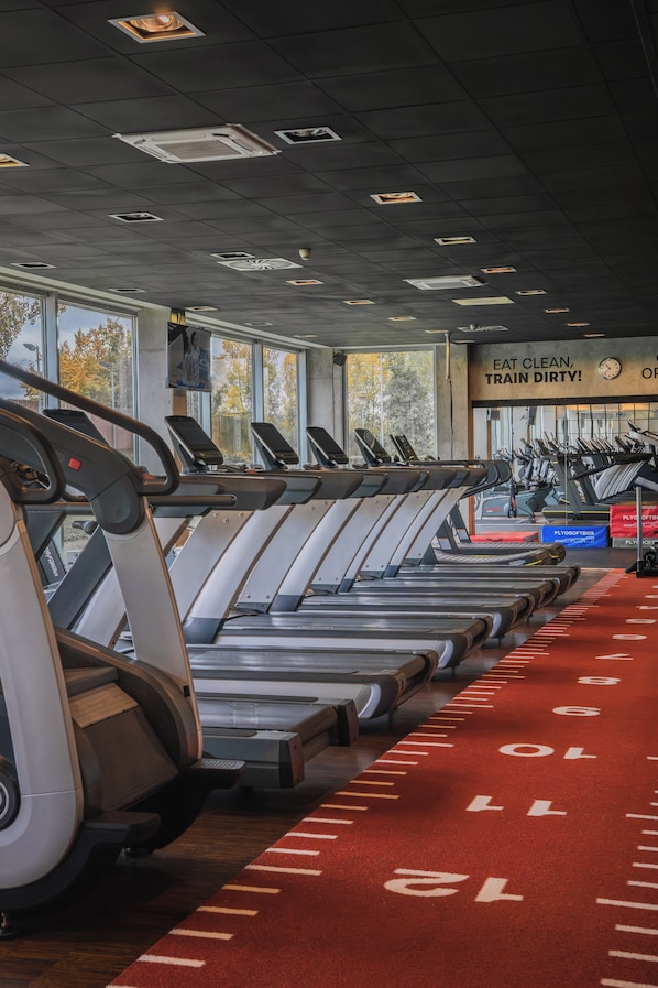 A gym with treadmills aligned in rows, a red running track, and a motivational poster on the wall.