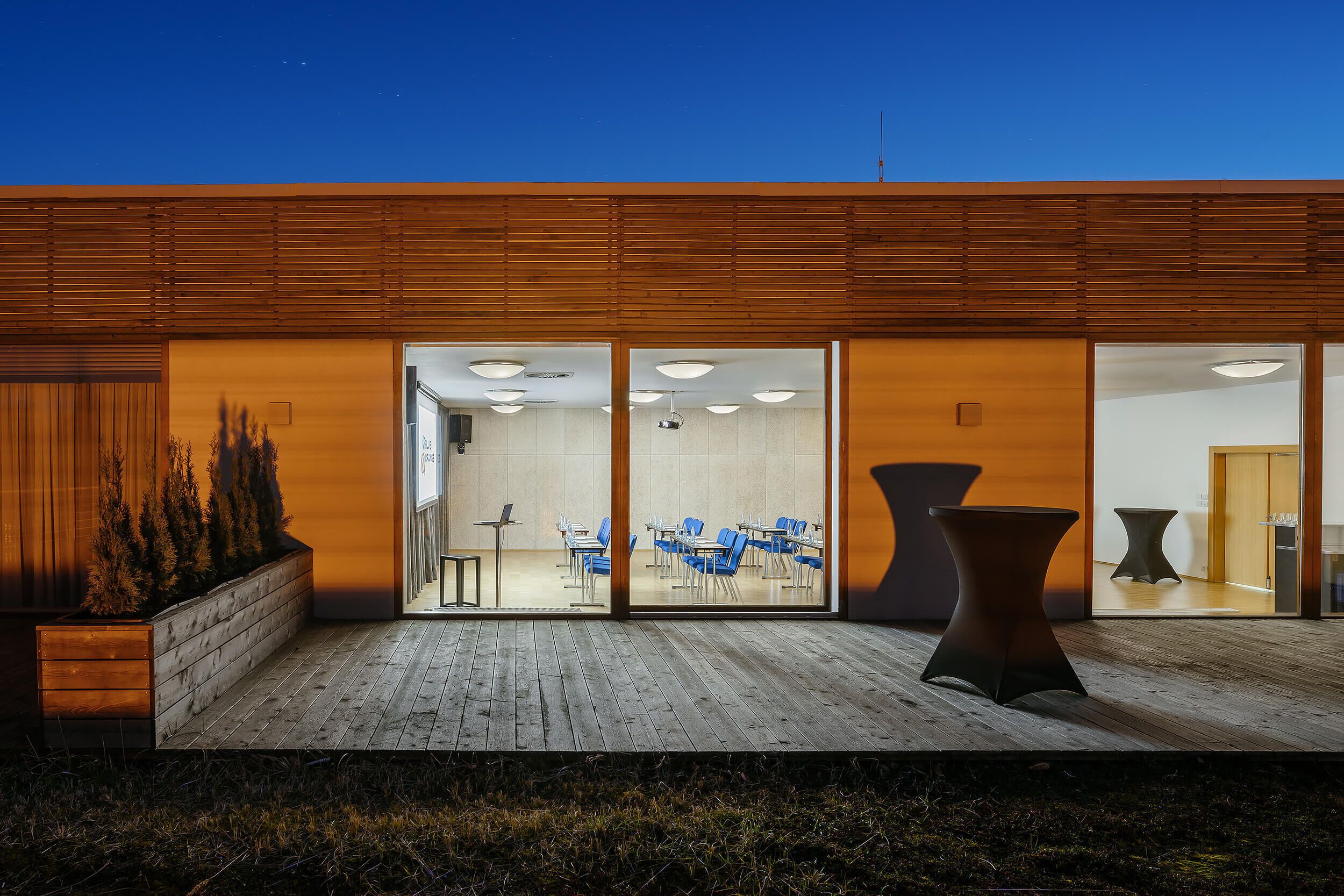 A modern building with a wooden facade, a glass entrance, and a seating area with tables and chairs.