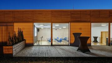 A modern building with a wooden facade, a glass entrance, and a seating area with tables and chairs.