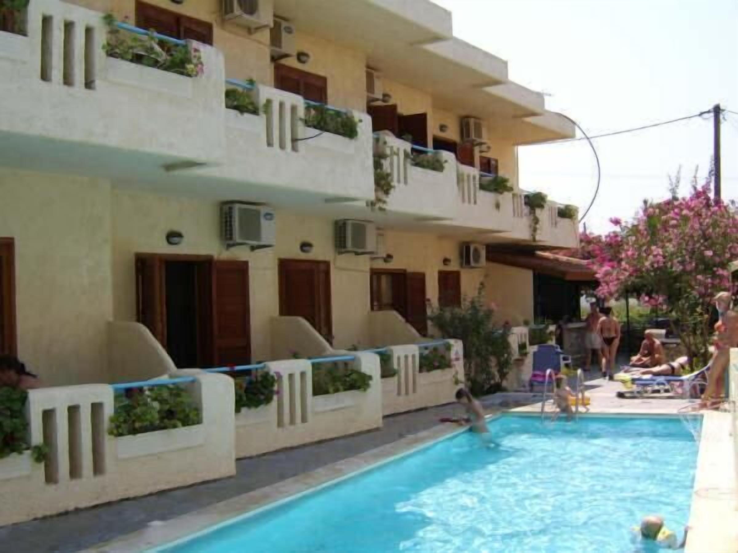 A swimming pool with a clear blue water surface, surrounded by a building with balconies and air conditioning units.