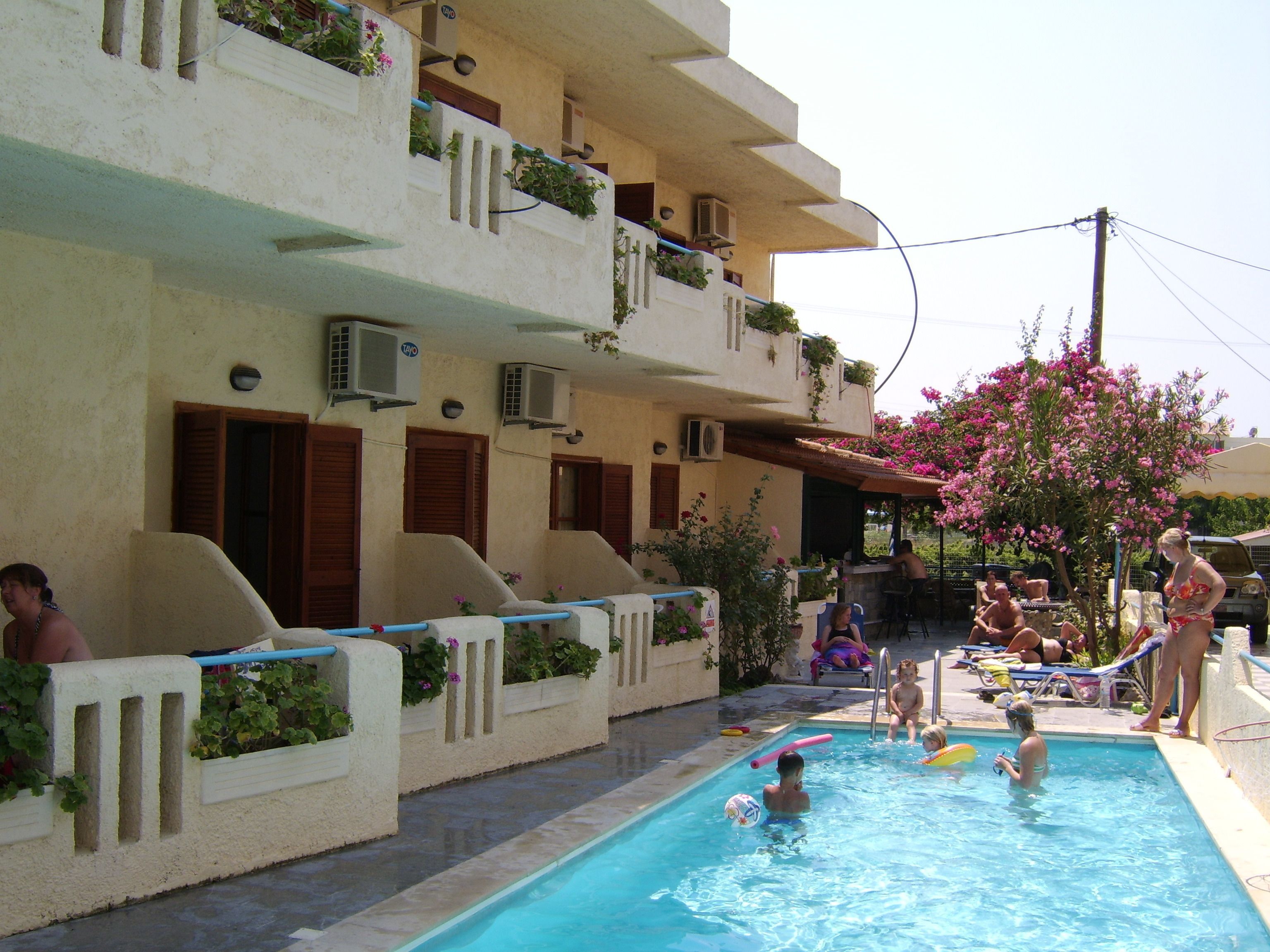 A swimming pool area with a pool, lounge chairs, and a building with balconies.