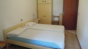A bedroom with a double bed, a wooden wardrobe, a wooden chair, and a wooden door.