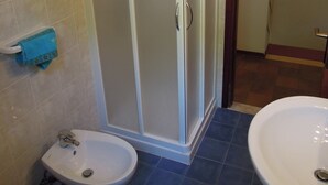 A bathroom with a shower enclosure, a bidet, and two sinks.