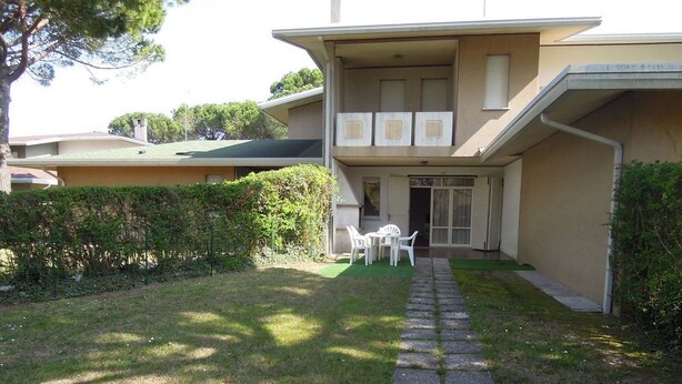 A two-story building with a paved pathway leading to a small patio area with outdoor furniture.