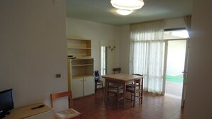 A room with a dining table, chairs, a TV, and a small cabinet.
