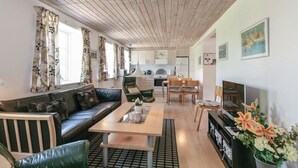 Un salon moderne avec un canapé, une table basse et une cheminée. On aperçoit une cuisine à l’arrière-plan, avec des placards et une cuisinière.