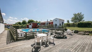 Une terrasse en bois avec une piscine, un espace salon extérieur et un petit bâtiment.