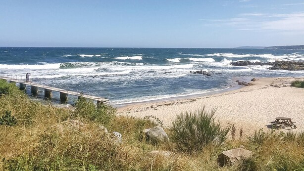 A beach with waves crashing onto the shore, a wooden pier extending into the water, and a sandy beach area with rocks and vegetation. - 2 bedroom gorgeous apartment in Allinge (Allinge)