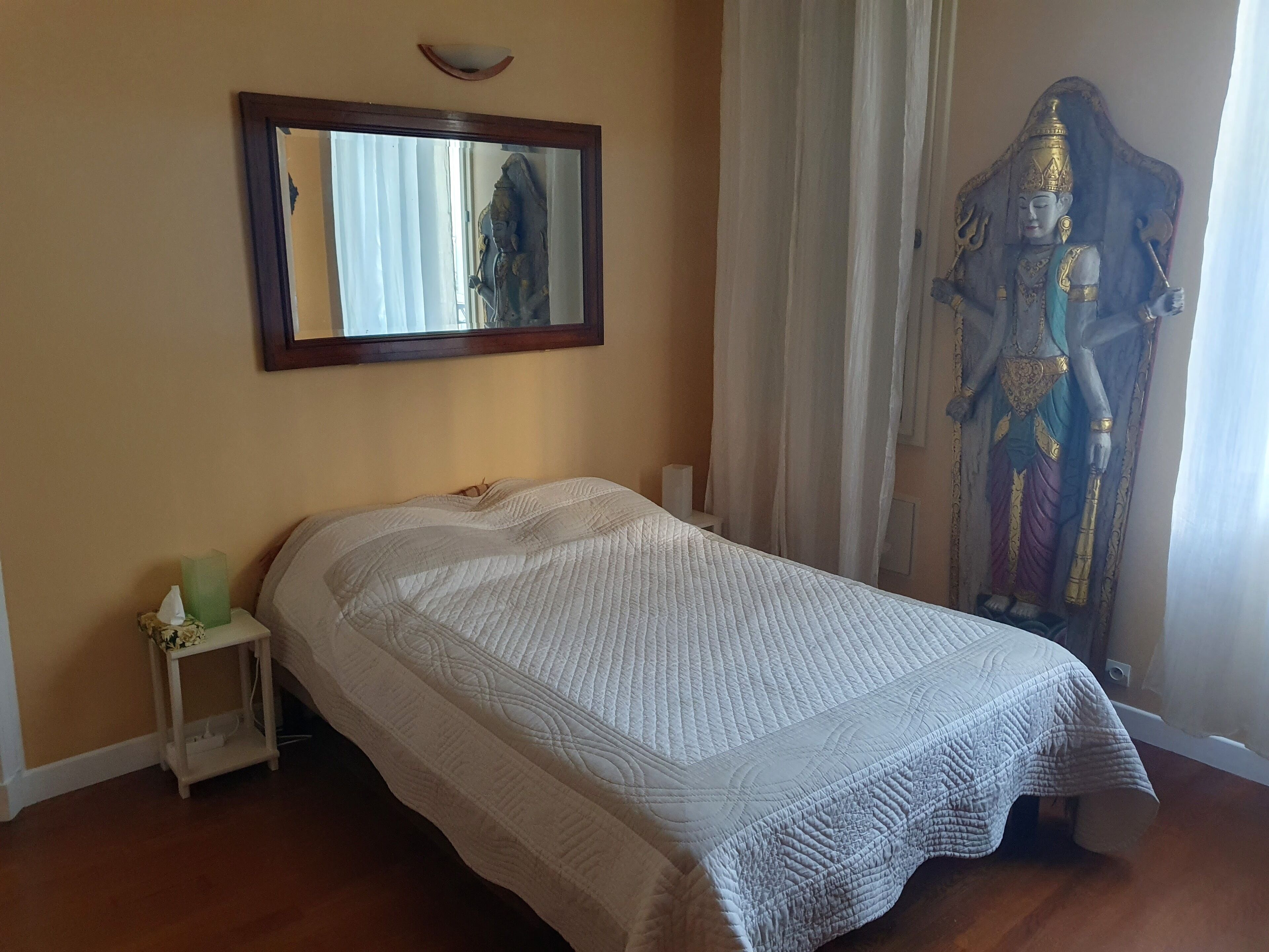 Ein Schlafzimmer mit einem Bett, einem Nachttisch, einem Spiegel und einer Statue.