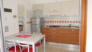 Une cuisine compacte avec des meubles blancs, un réfrigérateur, une cuisinière et un coin repas comprenant une table et des chaises.