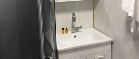 A bathroom with a glass shower enclosure, a white sink with a mirror above it, and a towel hanging on the wall.