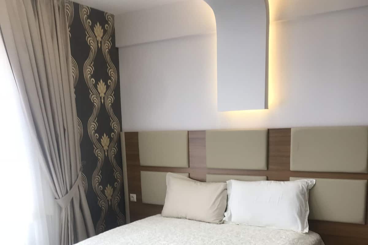 Ein Hotelzimmer mit einem großen Bett, einem Kopfteil mit einer Leuchte, einem Nachttisch und einem Vorhang.