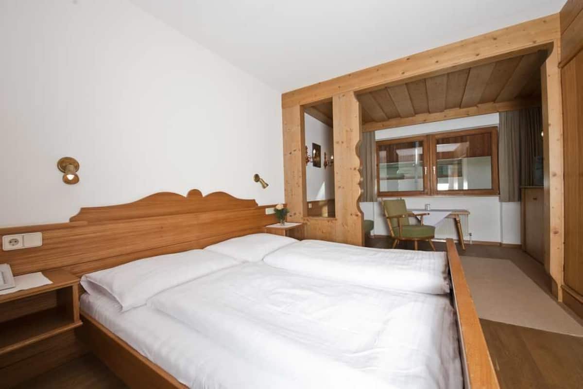 Een slaapkamer met houten frame, een bed, nachtkastje en een kleine stoel.
