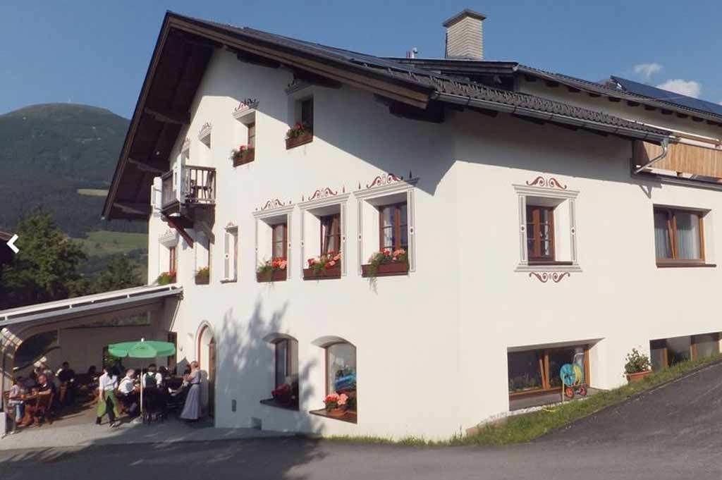 Ein weißes Gebäude mit zahlreichen Fenstern, von denen einige mit Blumenkästen versehen sind, und einer überdachten Außenbereich-Sitzgelegenheit.