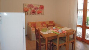 Een compacte keuken met een koelkast, een eettafel met stoelen, een bankje en een schilderij aan de muur.