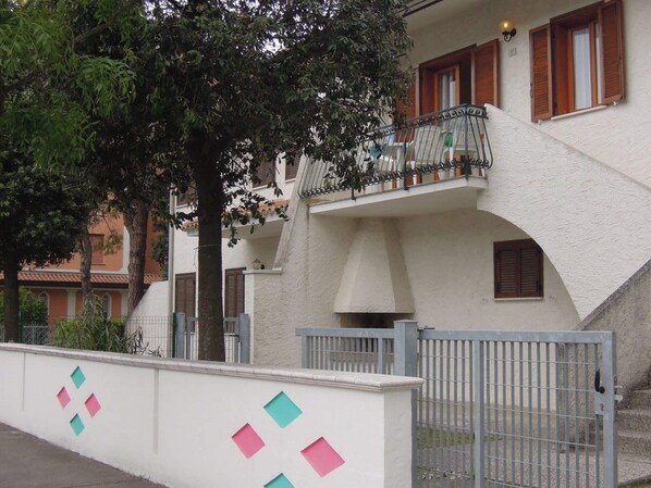 A two-story building with a balcony, a gated entrance, and a white wall with colorful geometric shapes.