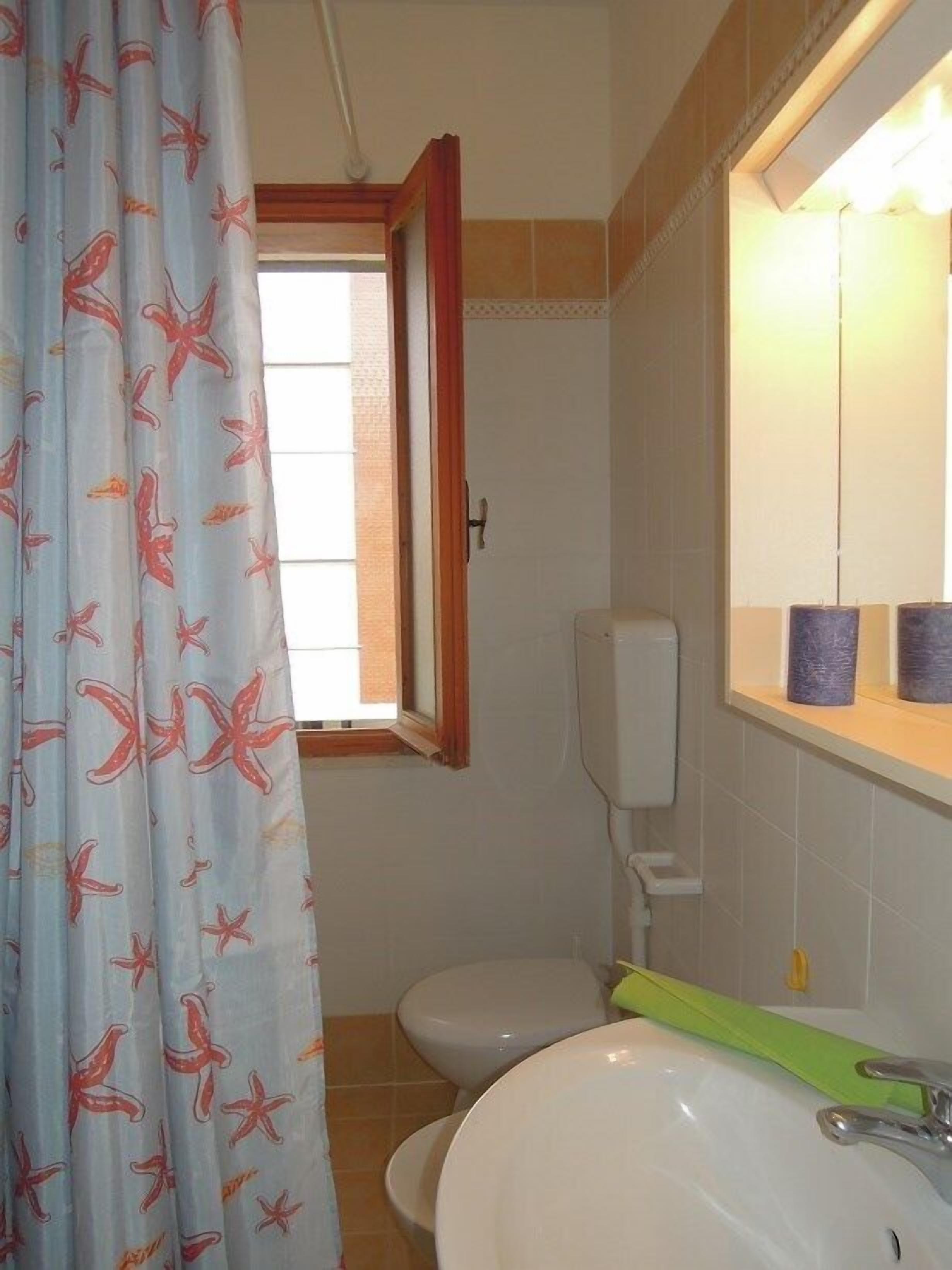 Ein Badezimmer mit Toilette, Waschbecken und einem Fenster mit Vorhang.